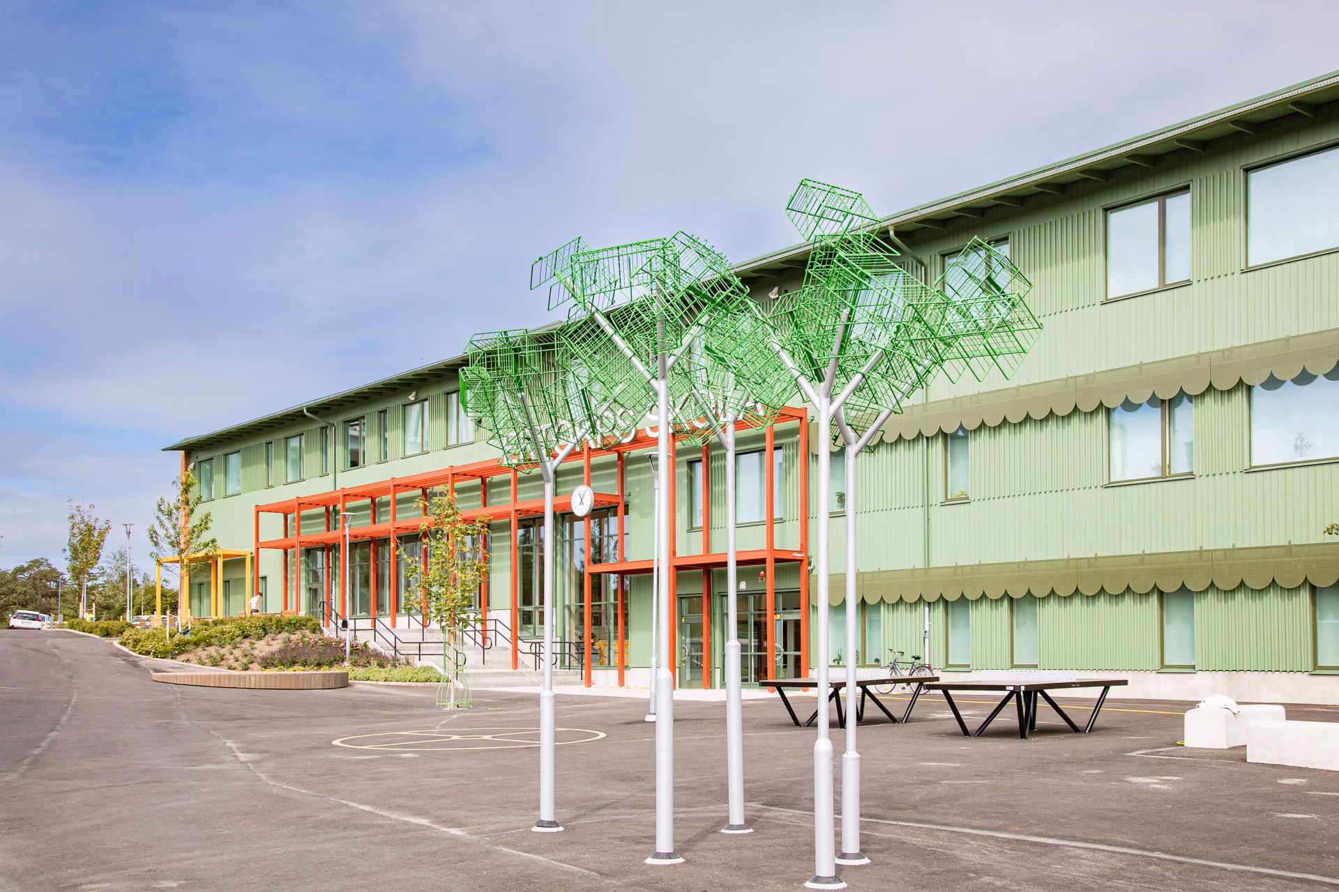 En skolbyggnad med återbrukskonst i form av träd i förgunden.